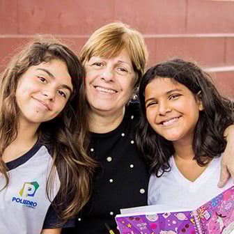 Mulher sorridente entre duas meninas alunas do Colégio Poliedro durante projeto Encontro de Gerações do Poliedro.