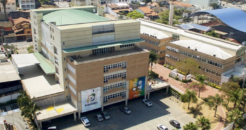 Vista aérea do Poliedro, edifício de múltiplos andares em área urbana, com estacionamento e quadra coberta ao fundo.