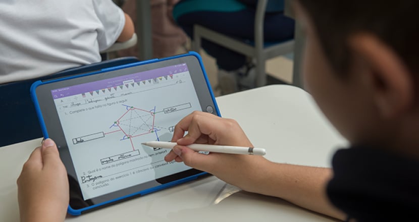 Aluno usando uma caneta digital para fazer atividade de geometria em um tablet na sala de aula.